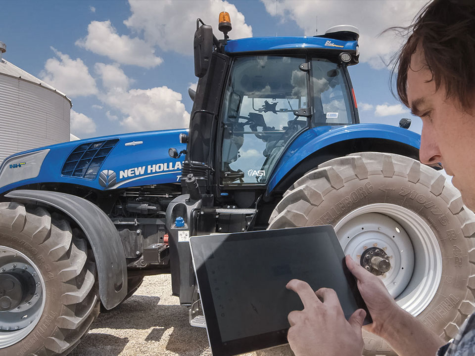 kundenservice mitarbeiter mit tablet vor blauem new holland traktor blauer himmel mit wolken