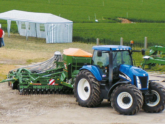 amazone bodenbearbeitungsgerät hinter blauem new holland traktor fährt auf feld