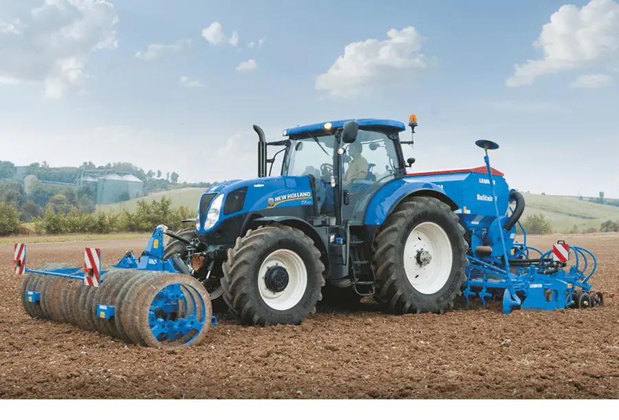 new holland traktor mit mulcher fährt über acker mit hügeln und silos im hintergrund