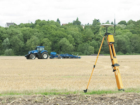 gps empfänger steht neben feld blauer new holland traktor mit pflug im hintergrund auf dem feldim einsatz