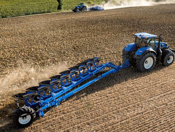blauer new holland traktor mit pflug fährt über acker