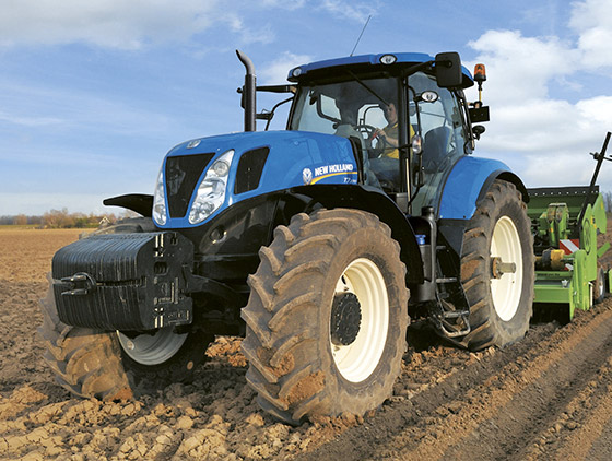 blauer new holland traktor auf acker mit grünem anbaugerät