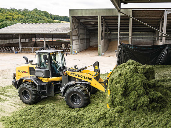 gelber new holland radlader schaufelt gemähtes gras auf hof