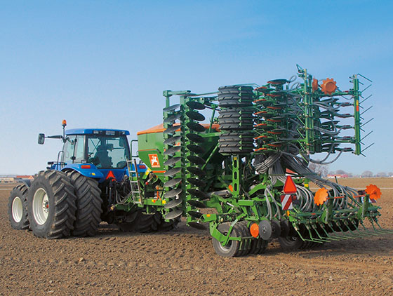 blauer traktor mit großer eingeklappter amazone säkombination fährt auf feld