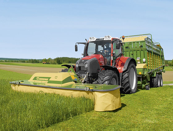 kron scheibenmähwerk schneidet hohes gras auf feld roter traktor blauer himmel