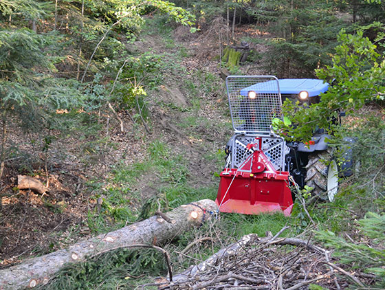 traktor mit roter unterreiner seilweinde zieht baumstamm durch wald