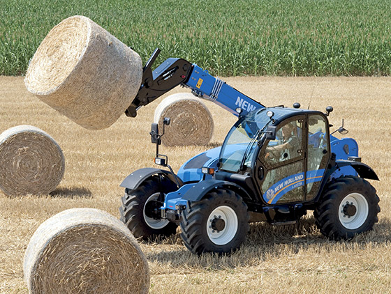 blauer new holland teleskoplader hebt rundballen auf feld